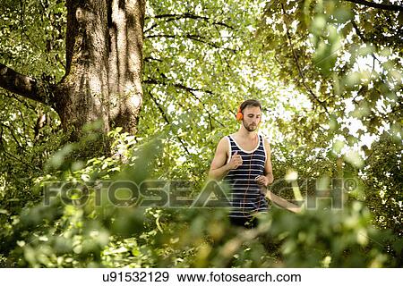 Young man in headphones running in woods View Large Photo Image Stock Photo - Young man in headphones running in woods. Fotosearch