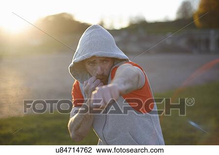 Stock Image - Young man in hooded top boxing training. Fotosearch