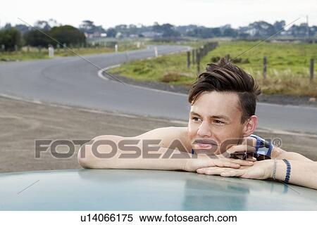 Stock Photography - Young man leaning on roof of vintage morris minor. Fotosearch