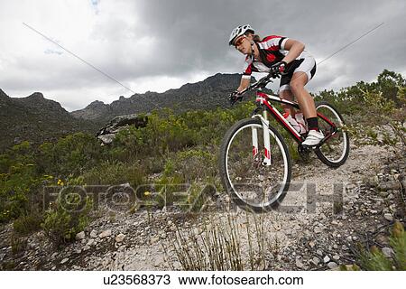 Stock Image - Young man mountain biking down mountain. Fotosearch