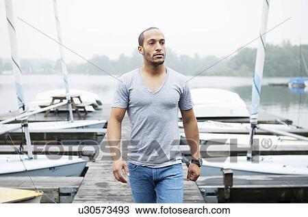 Stock Image - Young man on jetty in marina. Fotosearch