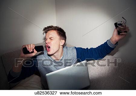 Young man singing into remote control on sofa View Large Photo Image Stock Photo - Young man singing into remote control on sofa. Fotosearch