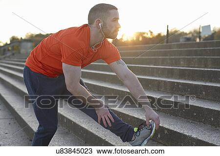 Stock Image - Young man stretching leg on step. Fotosearch