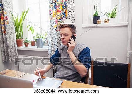 Young man using laptop and mobile with cup and saucer on his head View Large Photo Image Picture - Young man using laptop and mobile with cup and saucer on his head. Fotosearch