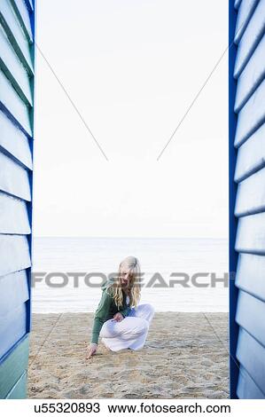 Stock Image - Young woman crouching between beach huts. Fotosearch