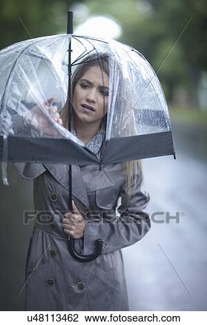Stock Image - Young woman looking at hole in umbrella. Fotosearch