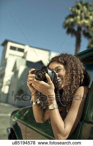 Stock Photo - Young woman photographing from car window. Fotosearch