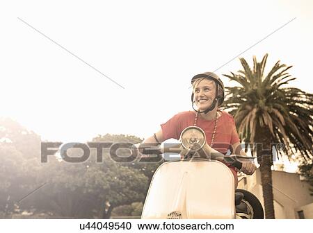 Stock Image - Young woman riding moped. Fotosearch