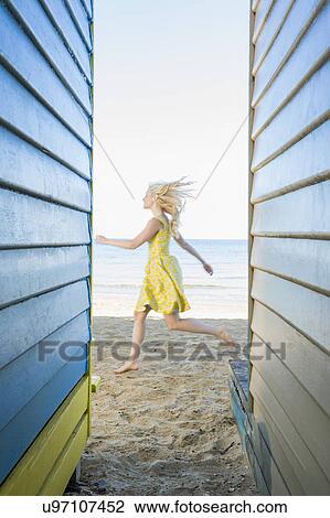 Stock Image - Young woman running between beach huts. Fotosearch