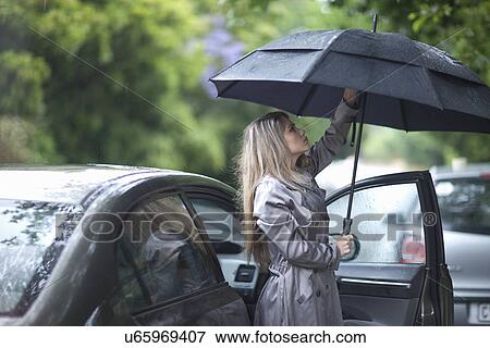 Stock Photo - Young woman struggling to put up umbrella. Fotosearch