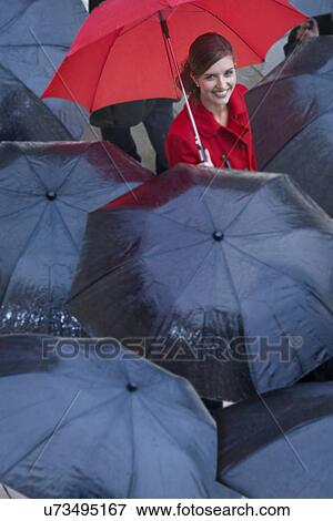 Stock Photo - Young woman with red umbrella amongst black umbrella's. Fotosearch