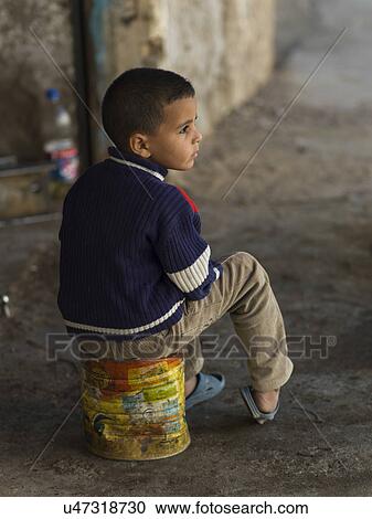 Stock Image - Boy sitting on a container, Tamzawrout, Morocco. Fotosearch