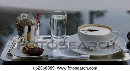 Stock Photo - Close-up of Cappuccino with cookies and glass of water on a tray, Marrakesh, Morocco. Fotosearch