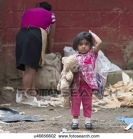 Girl holding a toy with her mother working in background, Finca El Cisne, Honduras View Large Photo Image Stock Image - Girl holding a toy with her mother working in background, Finca El Cisne, Honduras. Fotosearch