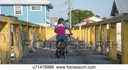 Stock Photo - Girl riding a tricycle on the bridge, Cayman Cay, Utila Island, Bay Islands, Honduras. Fotosearch