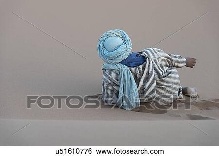 Stock Photograph - Man reclining on Erg Chegaga Dunes in Sahara Desert, Souss-Massa-Draa, Morocco. Fotosearch