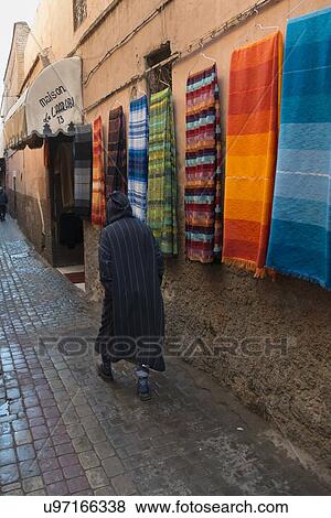 Stock Photo - Man walking along hanging carpets for sale on street, Medina, Marrakesh, Morocco. Fotosearch
