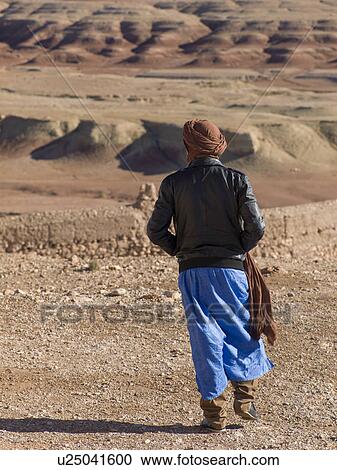 Stock Image - Tuareg man looking at a town view from the terrace of a fort, Ait Benhaddou, Ouarzazate, Souss-Massa-Draa, Morocco. Fotosearch
