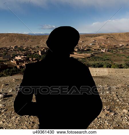 Stock Image - Tuareg man looking at a town view from the terrace of a fort, Ait Benhaddou, Ouarzazate, Souss-Massa-Draa, Morocco. Fotosearch