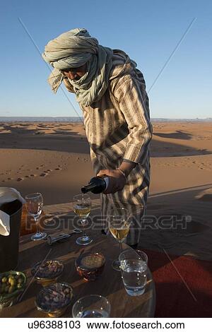 Stock Image - Tuareg man pouring wine in wineglass at Erg Chigaga Luxury Desert Camp in Sahara Desert, Souss-Massa-Draa, Morocco. Fotosearch