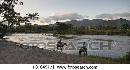 Stock Image - Two people riding horses at the lakeside, Copan, Copan Ruinas, Copan Department, Honduras. Fotosearch