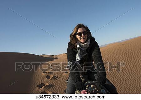 Stock Image - Woman riding a camel in Erg Chegaga Dunes, Sahara Desert, Souss-Massa-Draa, Morocco. Fotosearch