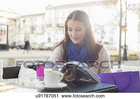 Stock Image - Beautiful woman reading book at sidewalk cafe. Fotosearch