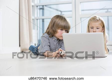 Boy and girl using laptop on floor at home View Large Photo Image Stock Photograph - Boy and girl using laptop on floor at home. Fotosearch