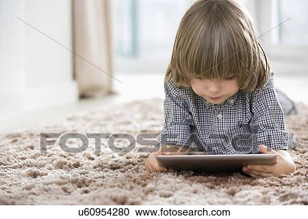 Stock Image - Boy using digital tablet while lying on rug at home. Fotosearch