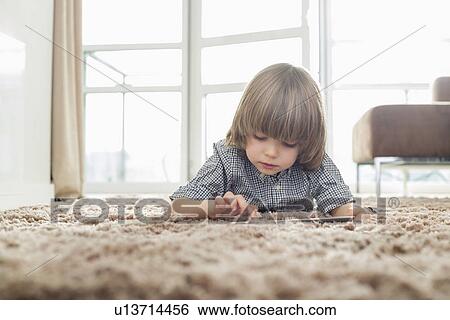 Boy using digital tablet while lying on rug in living room View Large Photo Image Stock Photograph - Boy using digital tablet while lying on rug in living room. Fotosearch