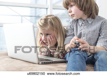 Stock Image - Brother and sister looking at laptop in living room. Fotosearch