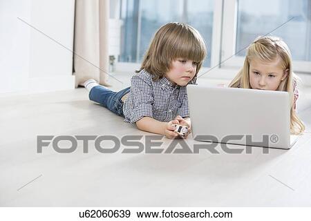 Brother and sister using laptop on floor at home View Large Photo Image Stock Photo - Brother and sister using laptop on floor at home. Fotosearch