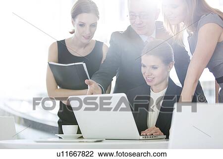 Stock Image - Business people discussing over laptop in office cafeteria. Fotosearch