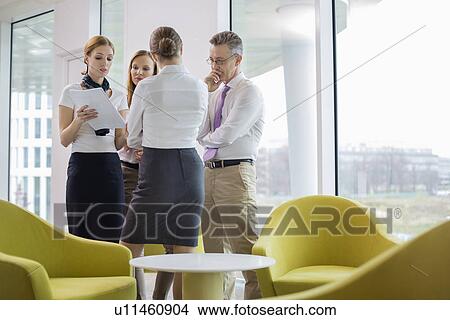 Business people discussing over documents in lobby View Large Photo Image Picture - Business people discussing over documents in lobby. Fotosearch