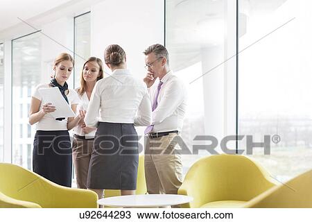 Stock Image - Business people discussing over documents in office lobby. Fotosearch