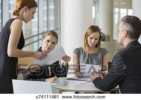 Stock Image - Business people doing paperwork in office cafeteria. Fotosearch