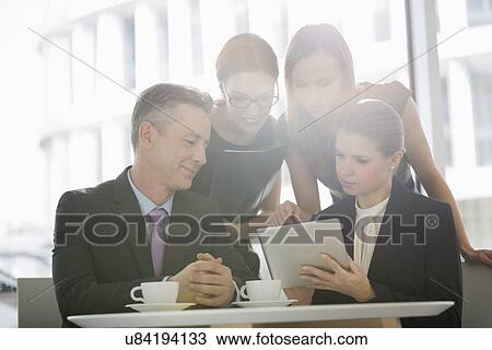 Stock Image - Business people using digital tablet together in office cafeteria. Fotosearch