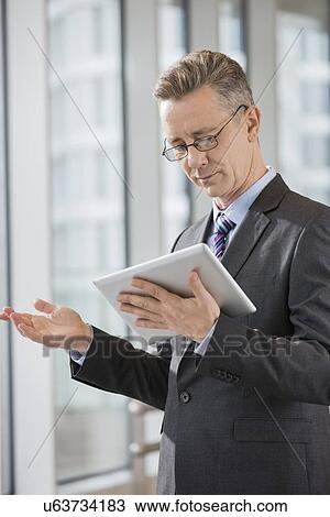 Businessman gesturing while using tablet PC in office View Large Photo Image Stock Image - Businessman gesturing while using tablet PC in office. Fotosearch