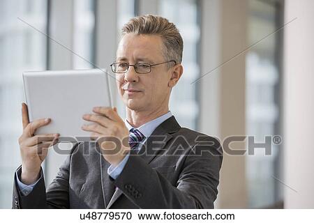 Businessman looking at digital tablet in office View Large Photo Image Stock Image - Businessman looking at digital tablet in office. Fotosearch