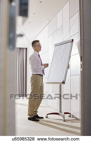 Stock Photo - Businessman looking at flipchart in office. Fotosearch