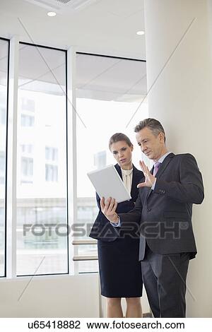 Businessman using digital tablet with female colleague in office View Large Photo Image Stock Image - Businessman using digital tablet with female colleague in office. Fotosearch