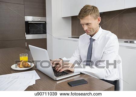Stock Photo - Businessman using laptop at breakfast table. Fotosearch