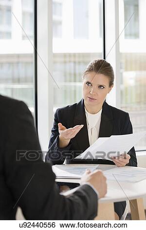 Stock Photograph - Businesswoman discussing over documents with colleague in office cafe. Fotosearch