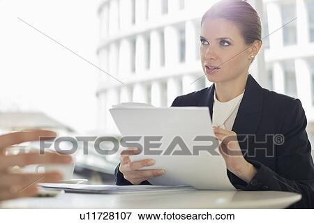 Stock Photo - Businesswoman discussion paperwork with colleague in office cafeteria. Fotosearch