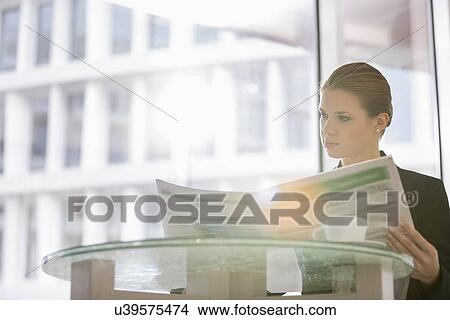 Picture - Businesswoman reading newspaper at office cafeteria. Fotosearch