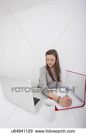 Businesswoman taking notes while looking at laptop in office View Large Photo Image Stock Photo - Businesswoman taking notes while looking at laptop in office. Fotosearch