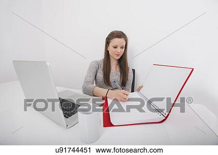 Stock Image - Businesswoman writing in book at office desk. Fotosearch