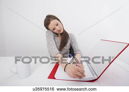 Businesswoman writing notes while answering smart phone in office View Large Photo Image Stock Photograph - Businesswoman writing notes while answering smart phone in office. Fotosearch
