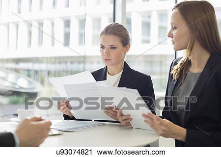 Businesswomen discussing over documents in office cafeteria View Large Photo Image Stock Image - Businesswomen discussing over documents in office cafeteria. Fotosearch