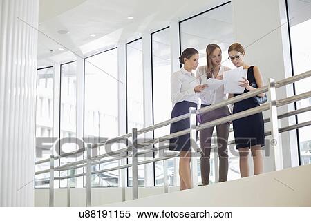 Stock Photography - Businesswomen discussing over paperwork against railing. Fotosearch